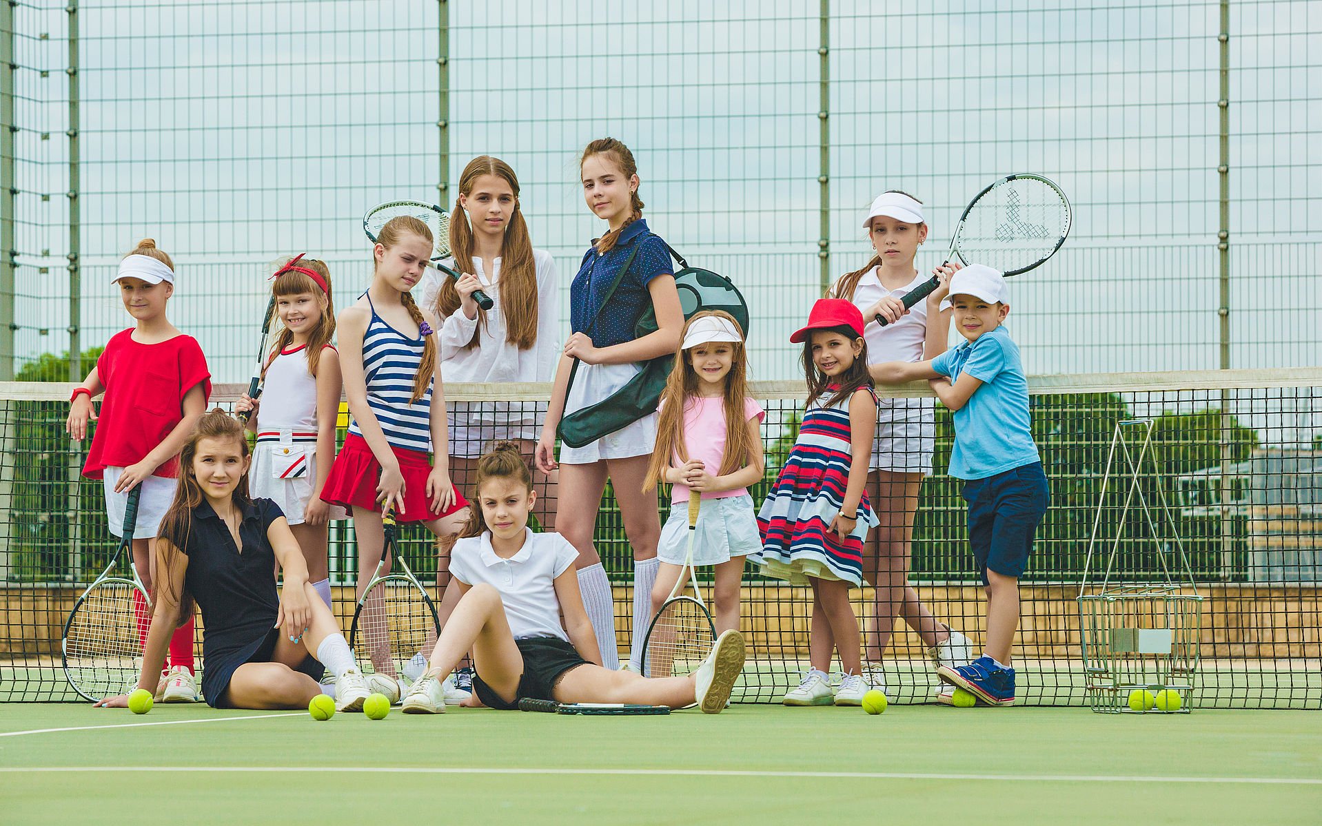 Portrait of group of girls as tennis players holding tennis racket against green grass of outdoor court